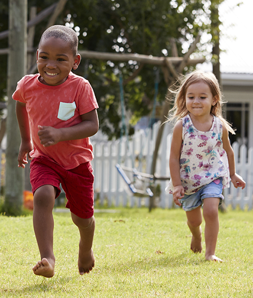 Två barn springer barfota på en gräsmatta.